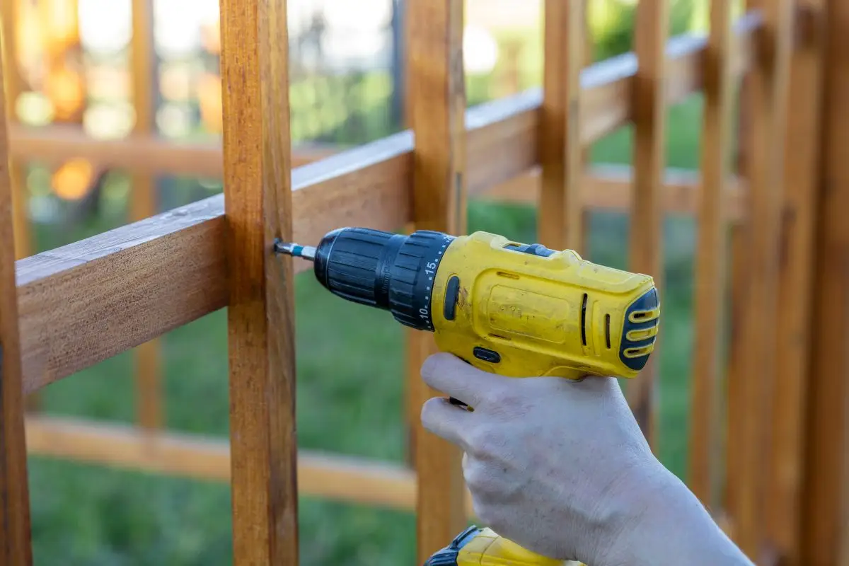 A person is using a drill to attach a wooden fence