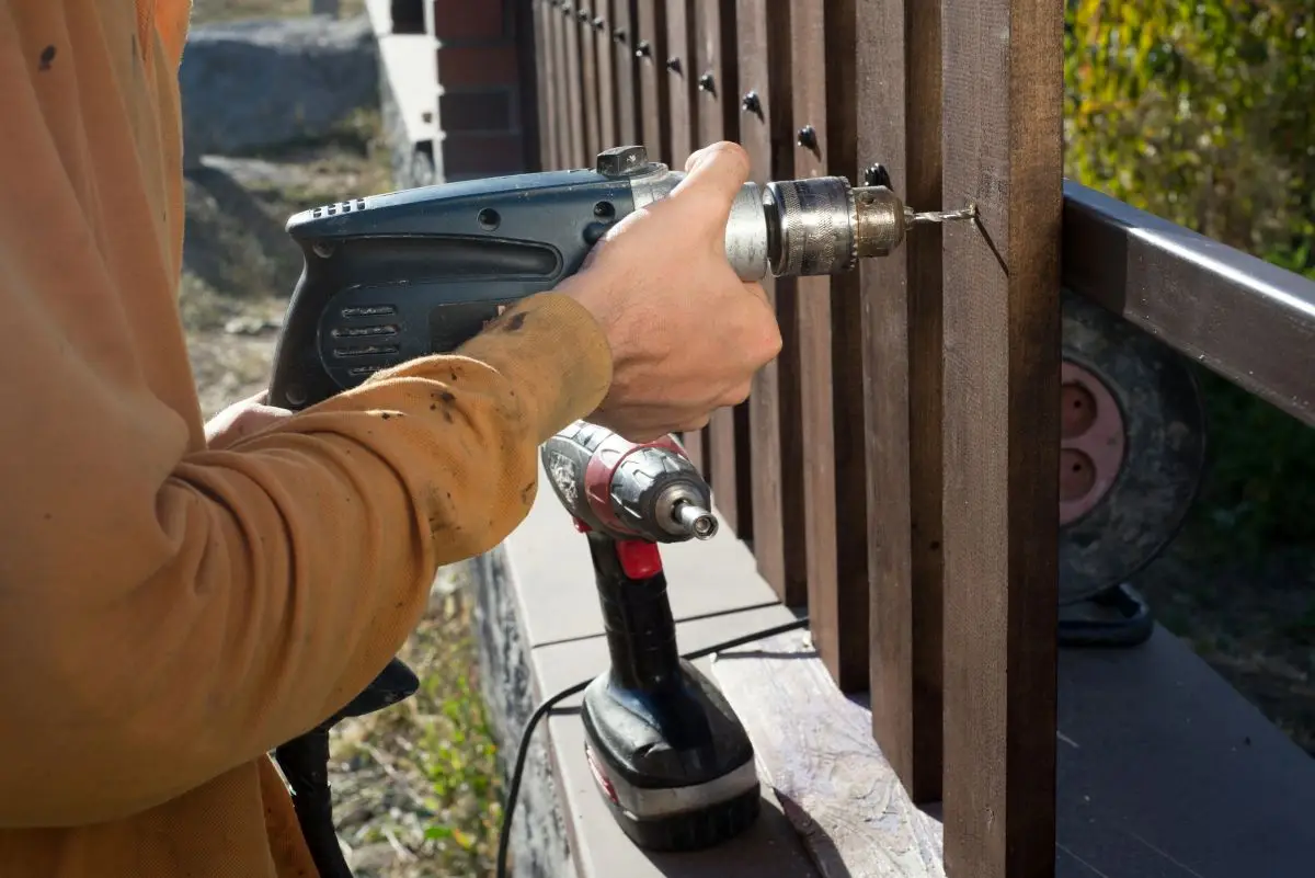 Man hands drilling wooden fence to metal construction