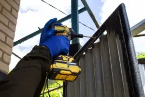 Power drill fastening metal gate during outdoor repair