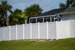 White vinyl picket fence on green lawn surrounding property grounds for backyard protection and privacy