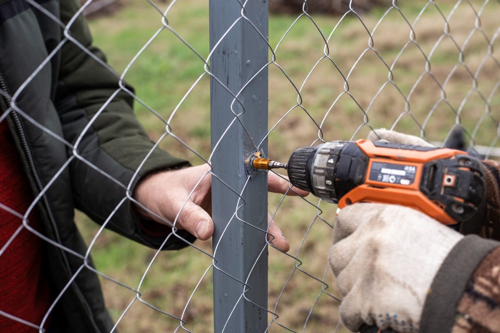 chain link fence installation worker using screwdriver to adjust fence