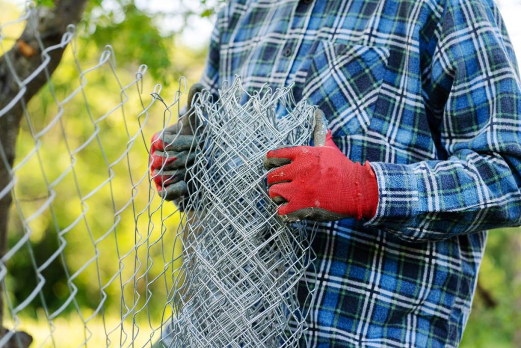chain link fence replacement Close up on midsection of unknown man holding protective chain link diamond wire fence in the field in day with copy space