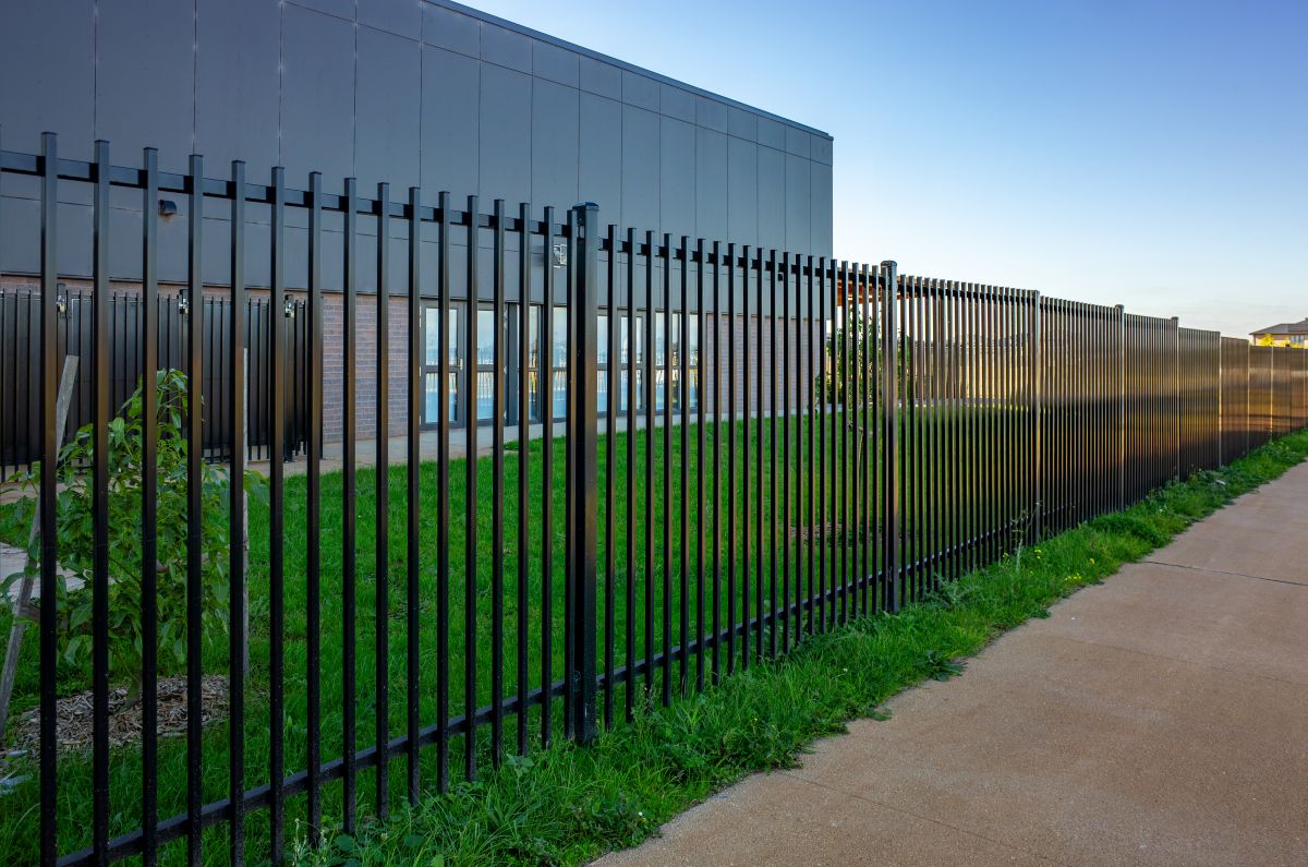 A black vertical metal security fence lines a path in front of a school building
