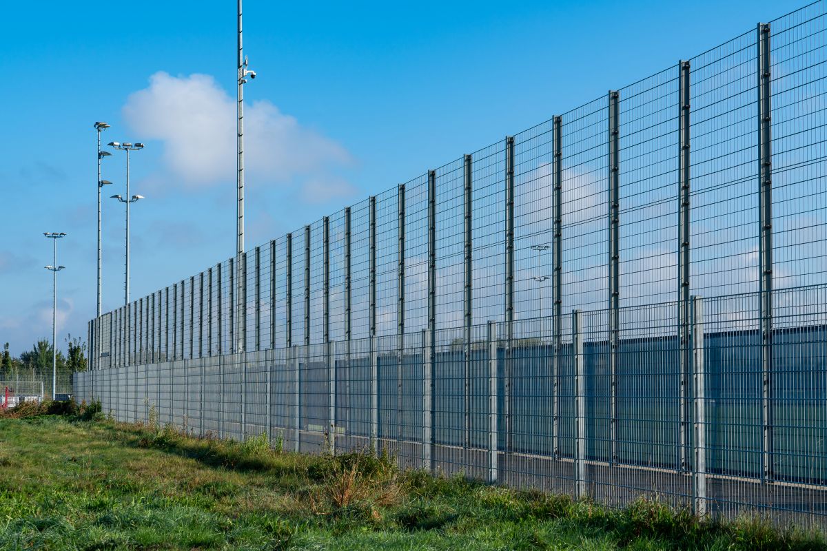 High security fence encompasses a facility, anchored by floodlights