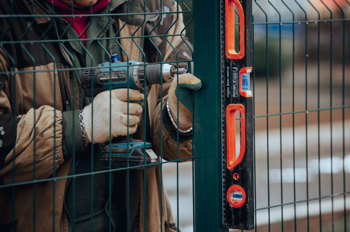 Worker installing metal fence using construction level tool